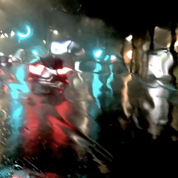 Œuvre photographique impressionniste de Sophie Moisan capturant une rue la nuit et une voiture qui passe nimbée de lumières colorées sous la pluie dans Cocktail de nuit.