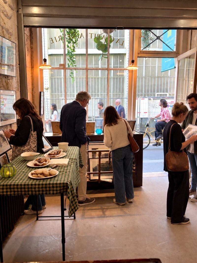 Visiteurs feuilletant et regardant les tirages encadrés de Sophie Moisan à l'intérieur de la galerie La Capitainerie de l'Isle, avec table de buffet au premier plan