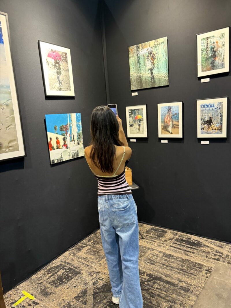 Visiteuse photographiant avec son téléphone les photographies d'art de Sophie Moisan, scènes de pluie à travers une vitre, sur le stand Artiti.art